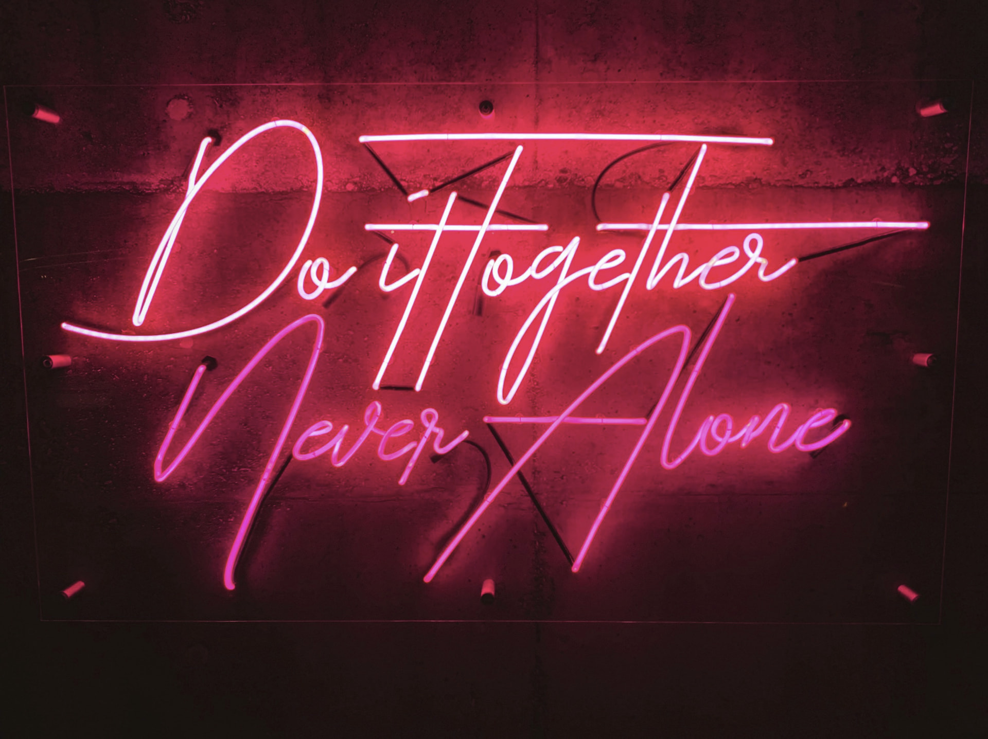 Glowing pink neon sign reading Do it together, never alone